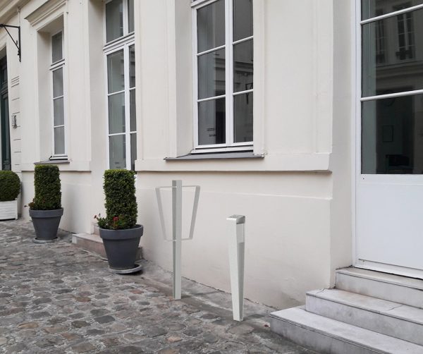 Une borne vélo et cendrier LUD gris incrustés sur le sol en pavés en pierre devant l'entrée d'un bâtiment